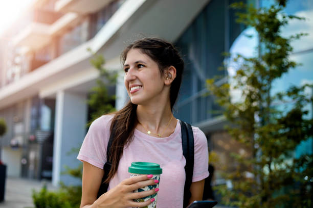 Teenage girl with hearing aid walking on city street Cheerful teenage girl with hearing aid walking on city street and using reusable coffee cup hearing aid stock pictures, royalty-free photos & images