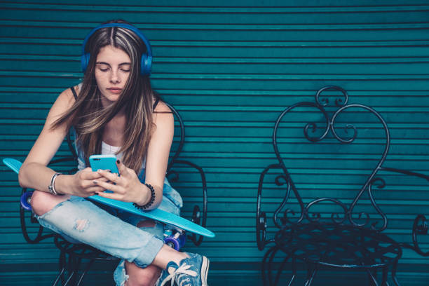 Teenage girl with skateboard texting Gen Z girl sitting against colorful wall and text messaging generation z stock pictures, royalty-free photos & images