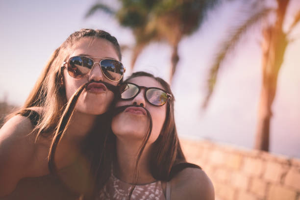 Teenage girls being silly making funny faces with hair mustaches Happy teenage best friends making funny faces and hair mustaches on tropical island summer holidays humor photos stock pictures, royalty-free photos & images