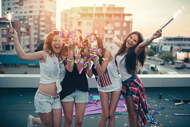 Teenage girls on a rooftop party Happy girls partying on a roof with confetti and sparklers new years eve girl stock pictures, royalty-free photos & images