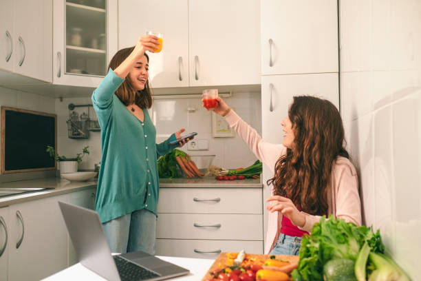 teenage girls toasting with fresh juices, while preparing a healthy meal, in the domestic kitchen stock photo