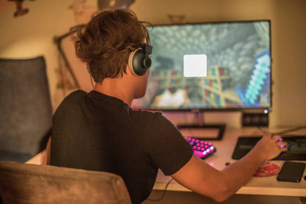 Teenager Boy Playing Multiplayer Video Game on Computer Wearing Headphones stock photo