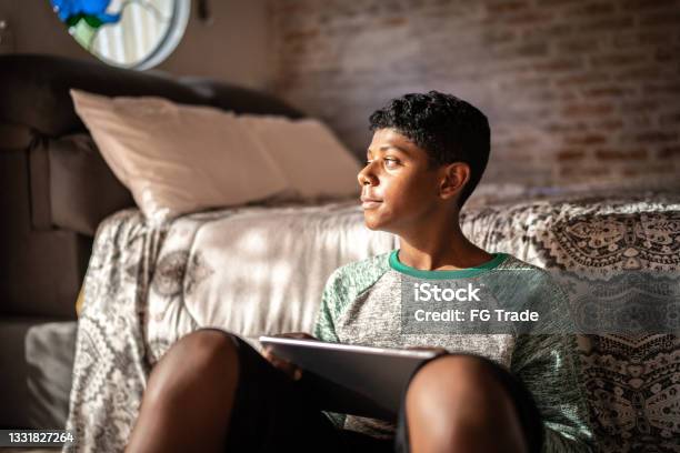 Teenager boy using digital tablet and contemplating at home