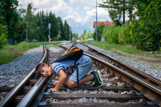 A teenager in summer clothes with a backpack sits  at the crossroads of railway tracks and sadly and absently observes the surroundings. stock photo
