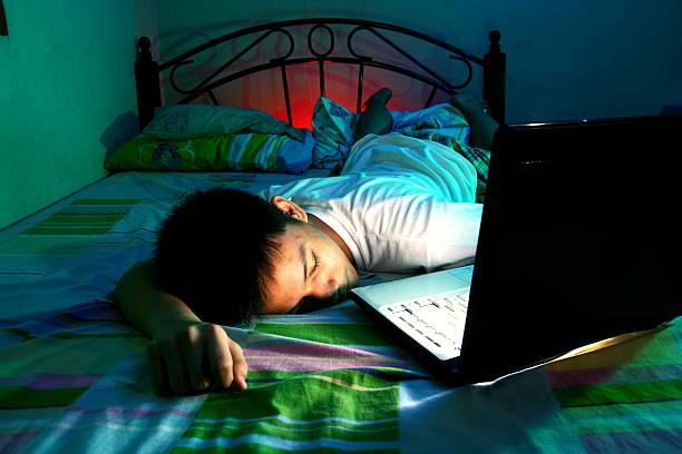 Teenager sleeping in front of a computer on a bed stock photo