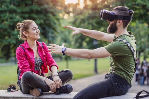 Teenager watching virtual reality with 3D glasses in the park Cheerful teenage couple enjoying virtual reality on 3D glasses and sitting in the park Portable DVD Player stock pictures, royalty-free photos & images