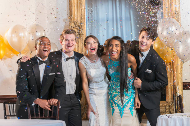 Teenagers and young adults in formalwear at party A group of five multi-ethnic teenagers and  young adults dressed in formalwear - dresses and tuxedos. They are at a special event, perhaps a prom or new year's eve party, confetti in the air. new years eve girl stock pictures, royalty-free photos & images