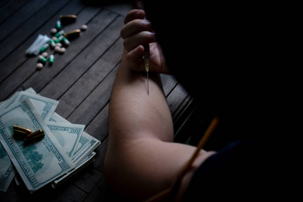 Teenagers are injecting drugs into their arms.
Mistake, drug addiction, obsession with evil
On the table are drugs, bankroll, gunshots. stock photo