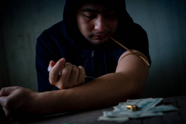 Teenagers are injecting drugs into their arms. Mistake, drug addiction, obsession with evil On the table are drugs, bankroll, gunshots. stock photo