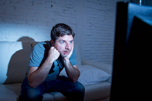 television addict man watching tv holding remote control mesmerized stock photo