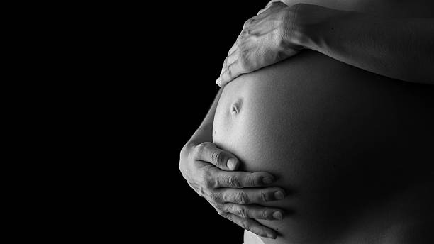 Tender pregnancy Greyscale image of woman tenderly holding her pregnant belly attentively turning to her unborn child. human abdomen stock pictures, royalty-free photos & images