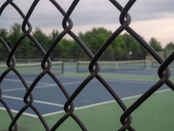 Tennis courts in background with black fence framing in foreground Some tennis courts in background with black fence framing in foreground linkage effect stock pictures, royalty-free photos & images
