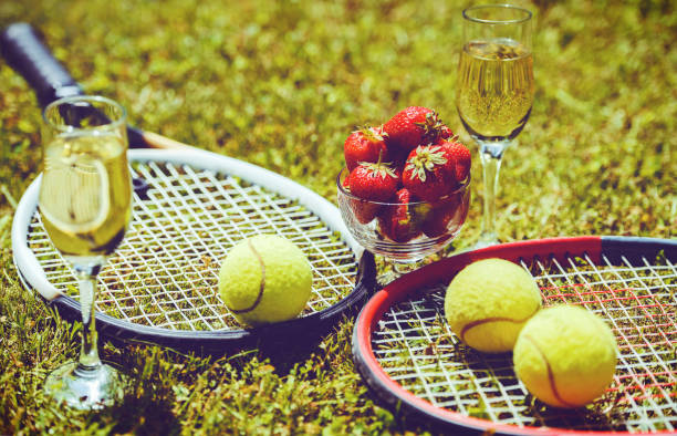 Tennis game. Strawberries, champagne and tennis balls with rackets on the green grass. Sport, recreation concept stock photo