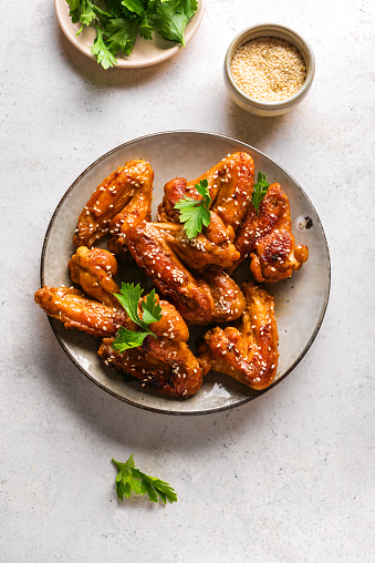 Teriyaki chicken wings with sesame and greens on white background, top view, copy space. Asian style meal - roasted chicken wings with teriyaki sauce.