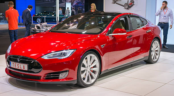Tesla Model S P90D full electric luxury car Brussels, Belgium - Januari 12, 2016: Red Tesla Model S P90D full electric luxury car front view. The P90D is fitted with All Wheel Drive and combines a front and rear axle power to a total of 762 horsepower for a 0-60 mph time of 2.8 sec. The car is on display during the 2016 Brussels Motor Show. The car is displayed on a motor show stand, with lights reflecting off of the body. There are people looking around and other cars on display in the background. tesla motors stock pictures, royalty-free photos & images