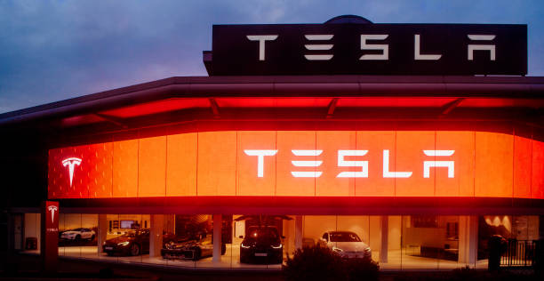 Tesla motors showroom with cars and illuminated logo branding at dusk London UK London:  View from the street  of modern Tesla Motors showroom with multiple luxury Tesla cars inside at sunset in central London tesla motors stock pictures, royalty-free photos & images