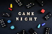 istock Text GAME NIGHT spelled out in wooden letter. Surrounded by dice, dominoes other game pieces on black background. Table games. Stay home activity 1312627888
