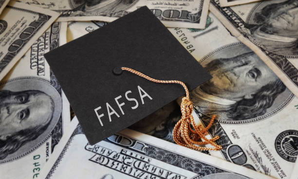 FAFSA (Free Application for Federal Student Aid) text on graduation cap and money - financial aid concept stock photo