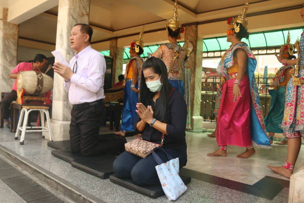 a thai couple praying at buddha eriwan shrine. the woman with corona mask - personne à genou en train de prier photos et images de collection