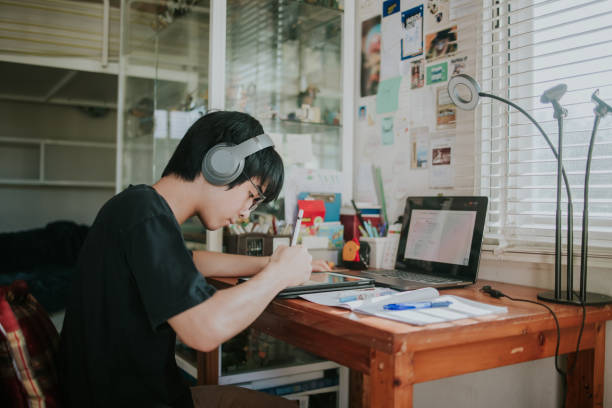 Thai nerd male teenager studying and doing school homework with tablet for Distance learning online education - stock photo stock photo