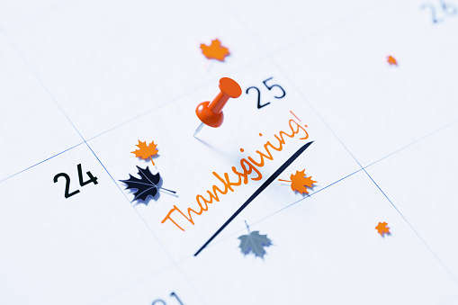 Thanksgiving note over white calendar pinned by orange push pin to remind its importance. Calendar and reminder concept. Horizontal composition with copy space. High angle view.