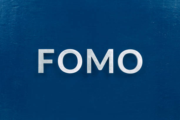 the abbreviation word fomo - fear of missing out - laid with silver letters on classic blue color flat surface The abbreviation word fomo - fear of missing out - laid with silver letters on classic blue color flat painted surface. Stock market or crypto trading concept. fomo photos stock pictures, royalty-free photos & images