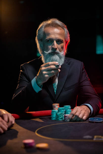 The bearded charming gray-haired men in the casino behind the gaming table are playing with gaming chips. stock photo