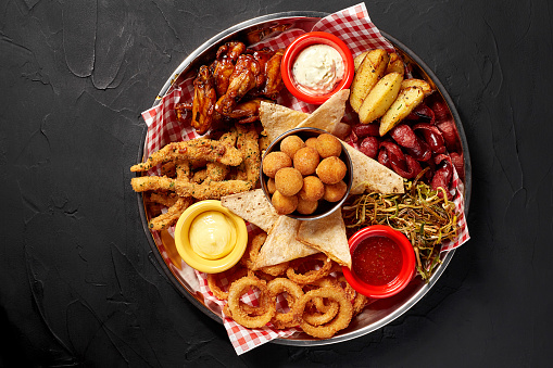 The beer plate with spicy chicken wings, calamari rings, fries onion rings, cheese balls, breaded, tartar sauce and garlic