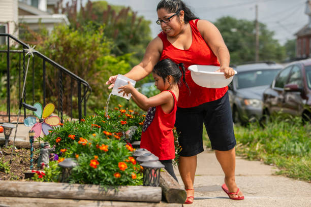 The big happy Latino, Mexican-American family. The little girl watering flowers nearby the porch, when her mother and sisters watching The big happy Latino, Mexican-American family. The little girl watering flowers outdoor, nearby the porch, when her mother and sisters watching. The sunny hot summer day at the parking lot nearby his house in Pennsylvania, USA hot latino girl stock pictures, royalty-free photos & images