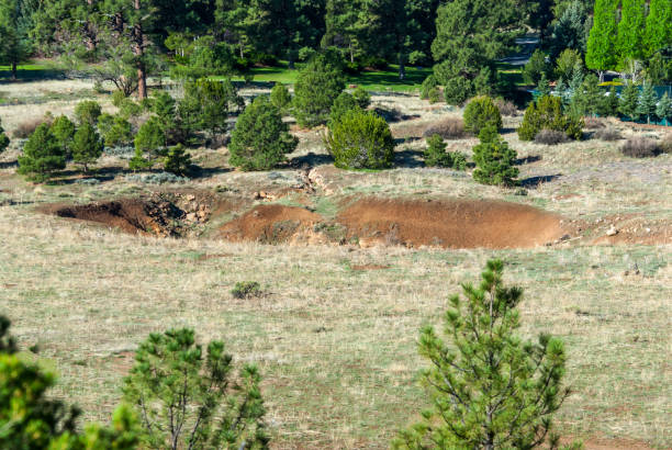 The Bottomless Pit The Bottomless Pit is a sinkhole in the Kaibab Limestone east of Flagstaff.  The sinkhole formed at the intersection of a long linear fault and a trench created by landforms moving away from each other.  Back in time there was probably a plug at the bottom of the pit which allowed a lake to form.  The plug eventually failed and the lake waters disappeared and left behind a sinkhole.  The pit most likely opened up around 1888 and has drawn rumors, intrigue and interest ever since.  Over time, the Bottomless Pit became a tourist attraction, luring visitors to stop on their way to Walnut Canyon National Monument.  There were even postcards published at the time showing an idealized version of the pit.  This view of the Bottomless Pit was photographed from Campbell Mesa in the Coconino National Forest near Flagstaff, Arizona, USA. jeff goulden stock pictures, royalty-free photos & images