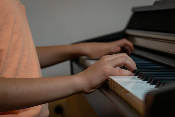 the boy plays the piano and lays his hands on the piano black and white keys stock photo