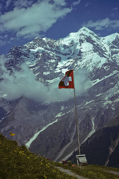 Swiss Flag and Breithorn The Breithorn, at 13,661 feet elevation, is a mostly glaciated peak lying on the border between Switzerland and Italy. The closest town is Zermatt in the Swiss Canton of Valais. The Breithorn which is German for “broad horn” is part of the Pennine Alps. Its highest peak is the Western Summit, whose first ascent was recorded in 1813. This photograph of the Breithorn with the iconic Swiss flag was taken from Obersteinberg in the Lauterbrunnen Valley of Bern Canton, Switzerland. jeff goulden scanned film stock pictures, royalty-free photos & images