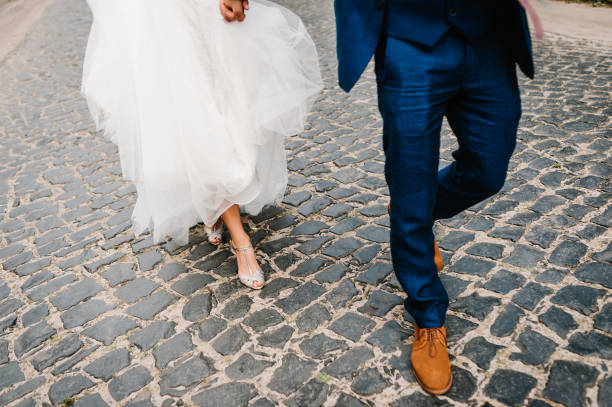 The bride and groom holding on hands and walking on road in the nature. Outdoors. Down view at shoes. stock photo