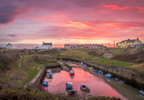 The Burn with the moored fishing boats of Seaton Sluice, Northumberland at sunrise The Burn with the moored fishing boats of Seaton Sluice, Northumberland at sunrise, with the fiery sky reflecting in the water northumberland stock pictures, royalty-free photos & images