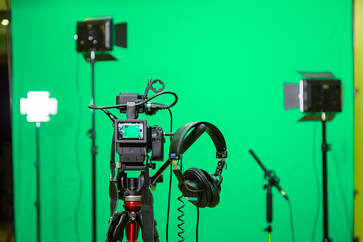 The camera on the tripod, led floodlight, headphones and a directional microphone on a green background. The chroma key. Green screen.