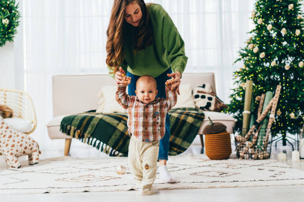 The child with the support of his mother takes the first steps. Christmas happy family moments. stock photo