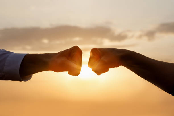 The concept of cooperation and teamwork in business. The concept of cooperation and teamwork in business. Two fists of businessmen on a background of the sun. dedication stock pictures, royalty-free photos & images
