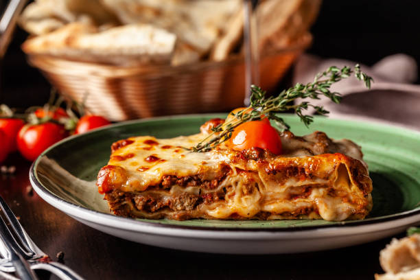 The concept of Italian cuisine. Baked lasagna with minced bolognese, pasta, cherry tomatoes lies on a green plate in a restaurant. A glass of red wine and bread basket on the table stock photo