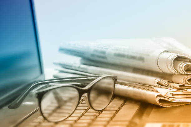 The concept of news. Folded stack of Newspapers on the laptop, eyeglasses. stock photo