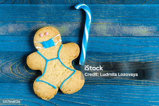 istock The concept of self-isolation. A cookie-cutter figure in a mask on a blue wooden background. Sweet dessert figure of a masked man 1317048126