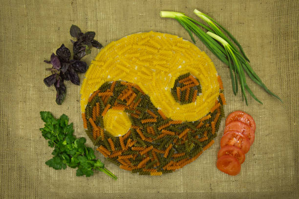 The concept of yin yang. Sign yin yang against the background of burlap. Colored pasta with natural dyes, green onion, tomatoes, parsley were used. stock photo