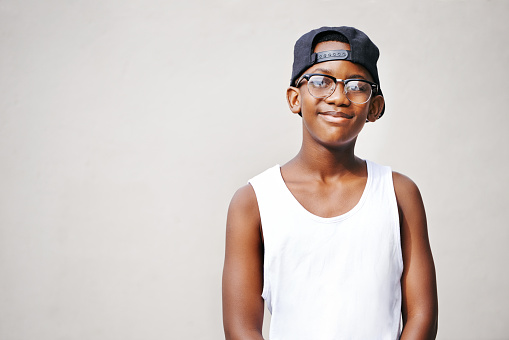 Portrait of a young boy wearing glasses and a cap posing against a gray background