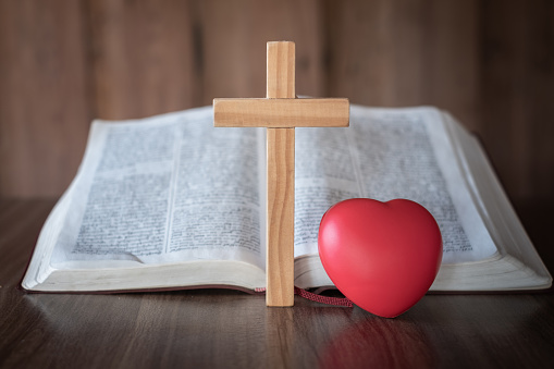 The cross and the red heart lay close together. Bible background and close-up images of the Lord Jesus' prayer Faith in the sacred power of God through prayer to Him, Christianity, Jesus.