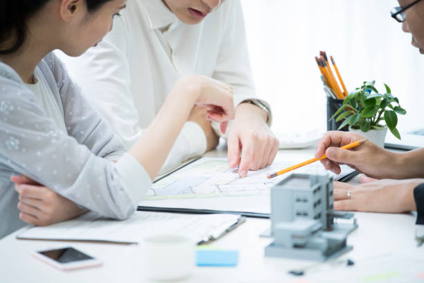 The customer and the employee are discussing the materials by looking at the materials. A couple and employees are talking while looking at the materials in the meeting table where the model of the house is placed. property management companies stock pictures, royalty-free photos & images