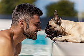 istock The dog and its owner are at the pool A smiling middle-aged man with a handsome face refreshes himself in the pool on a sunny summer day as he looks straight into the eyes of his dog lying by the pool 1334655812