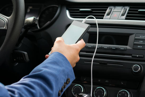 the driver of the vehicle, holds in his hand the phone connected by a white wire, to the car's music system the driver of the vehicle, holds in his hand the phone connected by a white wire, to the car's music system plug adapter stock pictures, royalty-free photos & images