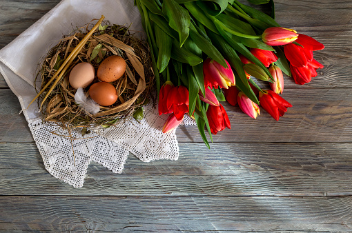 The easter composition. Eggs, a red tulips and church candles on wooden table close-up.