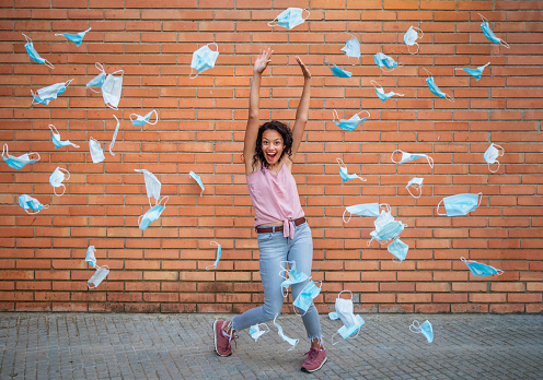 Young woman throwing masks in the air celebrating the end of coronavirus pandemic in front of a wall