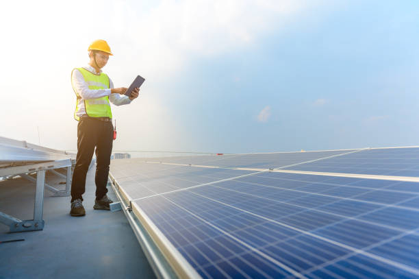 The engineer holding a tablet is checking the solar panel on the roof of the building to save energy. stock photo