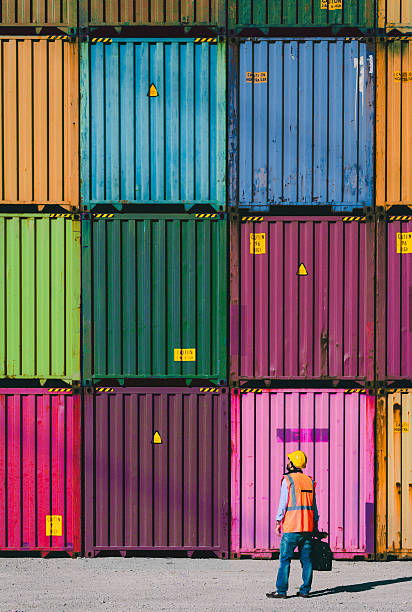 The engineer working with Cargo Containers Engineer man with yellow crash helmet and worker west checking cargo freights in front of colorful  cargo container stacks in shipping port barge stock pictures, royalty-free photos & images